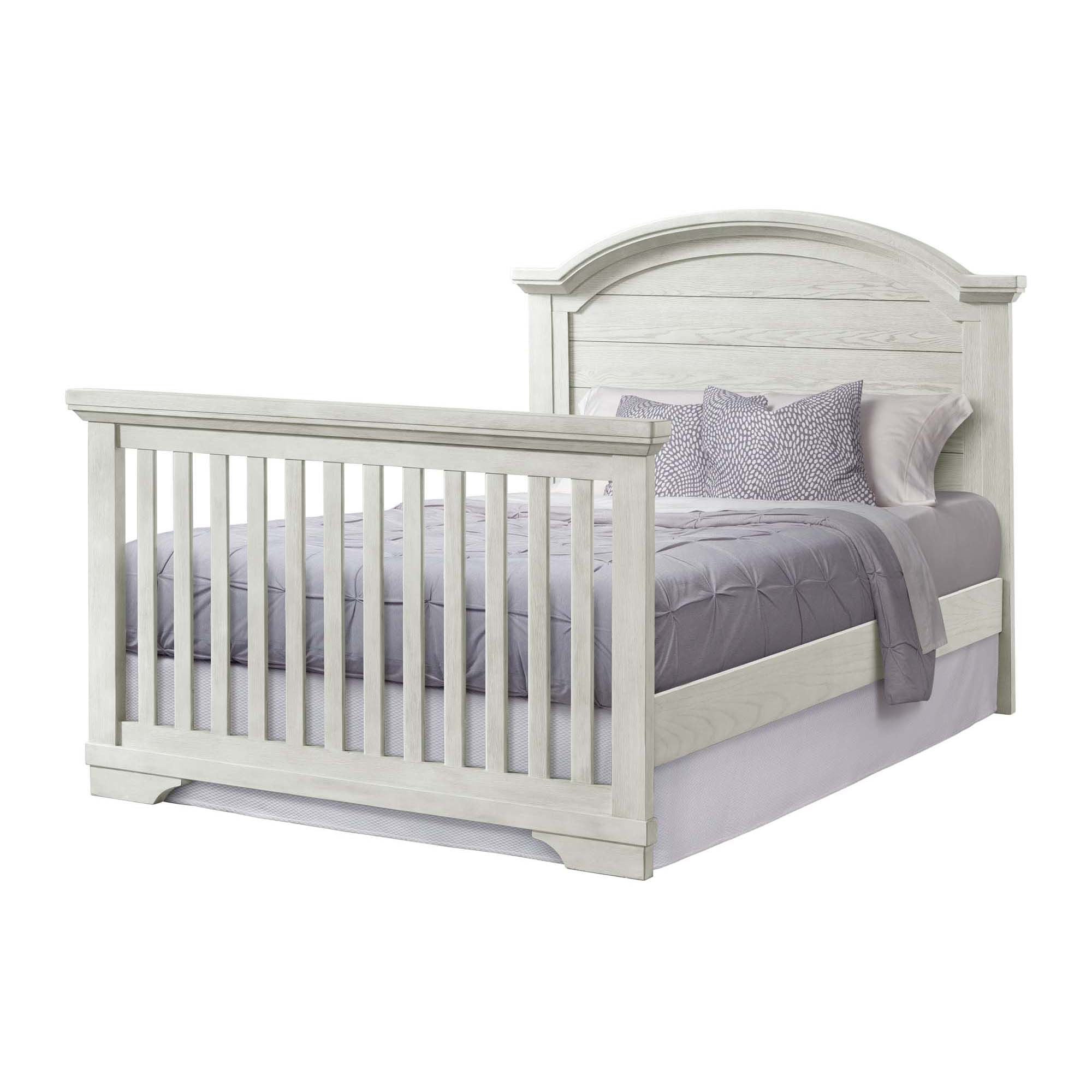 White wooden toddler bed frame with arched headboard and slatted rails, light gray bedding visible
